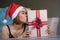 Young beautiful and happy woman in Santa hat holding and kissing Christmas present box with red ribbon smiling cheerful and excite