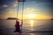 Young beautiful happy woman swinging on a swing on the beach during sunset, relaxing travel lifestyle concept