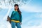 A young beautiful hipster woman poses with a skateboard in her hands. Blue sky in the background. Bottom view. Copy space. Concept