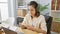 Young beautiful hispanic woman business worker watching video on smartphone using headphones at the office