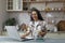 Young beautiful hispanic woman with curly hair working at home using laptop, woman in kitchen smiling and happy remote