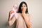 Young beautiful hispanic woman holding breast cancer awareness pink ribbon cover mouth with hand shocked with shame for mistake,