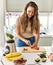 Young beautiful hispanic woman preparing vegetable smoothie with blender cutting strawberries at the kitchen