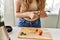 Young beautiful hispanic woman preparing vegetable smoothie with blender cutting strawberries at the kitchen