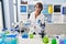 Young beautiful hispanic woman scientist pouring liquid on bottle at laboratory