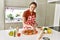 Young beautiful hispanic woman smiling confident putting onion on pizza at the kitchen