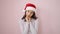 Young beautiful hispanic woman standing looking upset wearing christmas hat over isolated pink background