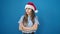 Young beautiful hispanic woman standing upset wearing christmas hat over isolated blue background