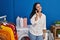 Young beautiful hispanic woman talking on smartphone waiting for washing machine at laundry room