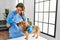 Young beautiful hispanic woman veterinarian measuring dog temperature holding thermometer at home