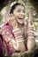 Young beautiful Indian Hindu bride laughing under tree with painted hands raised