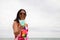 A young, beautiful Latina woman is holding a glass with a blue cocktail in it. The woman is on the beach wearing sunglasses. In