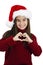 Young beautiful little girl wearing Christmas hat. Smiling in love showing heart symbol and shape with hands. Romantic concept.