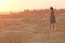 Young beautiful lonely smiling woman with long hair in long blue dress standing on sand at sunrise in hilly desert