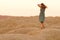 Young beautiful lonely woman with long hair in long blue dress dancing on sand at sunrise in hilly desert