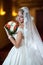 Young beautiful luxurious woman in wedding dress posing in luxurious interior. Bride with long veil holding her wedding bouquet