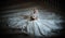 Young beautiful luxurious woman in wedding dress sitting on stair steps in semi-darkness. Bride with huge wedding dress