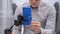 Young beautiful man wears gray shirt, black glasses look, hold blue phone on tripod close up. Male touch screen, typing