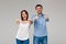 Young beautiful married couple posing, showing okay over grey background.