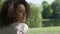 Young beautiful mixed race woman with curly afro hair smiling happily in a green park.