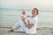Young beautiful mother and baby sitting on sandy beach looking at camera and smile