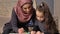 Young beautiful mother in hijab doing homework, little daughter paints with colored pencils, draws, children`s coloring