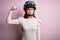 Young beautiful motorcyclist woman with blue eyes wearing moto helmet over pink background Strong person showing arm muscle,