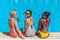 Young beautiful multiethnic women with cocktails sitting near swimming pool
