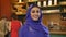 Young beautiful muslim woman in blue hijab standing in bakery shop and smiling at camera