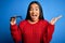 Young beautiful optical asian woman holding glasses over  blue background very happy and excited, winner expression