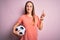 Young beautiful player woman playing soccer holding football ball  over pink background surprised with an idea or question