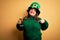 Young beautiful plus size woman wearing green hat celebrating st patricks day drinking beer with surprise face pointing finger to