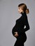 Young beautiful pregnant woman in black dress and massive cross earrings standing and looking down