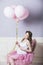 Young beautiful pregnant woman with pink balloons and a pink ballet skirt