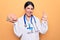 Young beautiful psychiatrist woman wearing stethoscope holding brain over yellow background doing ok sign with fingers, smiling
