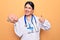 Young beautiful psychiatrist woman wearing stethoscope holding brain over yellow background smiling happy and positive, thumb up