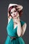 Young beautiful red-haired caucasian woman in aquamarine dress posing in studio on gray background, professional makeup and