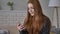 Young beautiful red-haired teen girl uses a smartphone, smiling, texting, scrolling, swiping, emotion of surprise, home