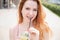 Young beautiful red-haired woman with braces drinks cooling cocktail outdoors in summer. Portrait of a smiling girl with