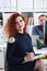 Young beautiful red haired woman sit at table in office in cabinet of her boss hold pen in arms