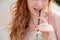 Young beautiful red-haired woman smiling with braces drinks cooling lemonade outdoors in summer. Cropped portrait Girl