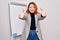 Young beautiful redhead businesswoman doing business presentation using magnetic board approving doing positive gesture with hand,