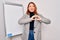 Young beautiful redhead businesswoman doing business presentation using magnetic board smiling in love doing heart symbol shape