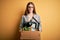 Young beautiful redhead businesswoman fired holding carboard box over yellow background with a confident expression on smart face