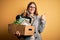 Young beautiful redhead businesswoman fired holding carboard box over yellow background happy with big smile doing ok sign, thumb