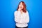 Young beautiful redhead businesswoman wearing elegant shirt standing over blue background thinking concentrated about doubt with