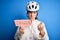 Young beautiful redhead cyclist woman wearing bike helmet holding danger paper message annoyed and frustrated shouting with anger,