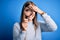 Young beautiful redhead detective woman using magnifying glass over isolated blue background stressed with hand on head, shocked