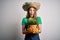 Young beautiful redhead farmer woman wearing apron and hat holding plant pot scared in shock with a surprise face, afraid and