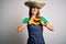 Young beautiful redhead farmer woman wearing apron and hat over white background smiling in love showing heart symbol and shape